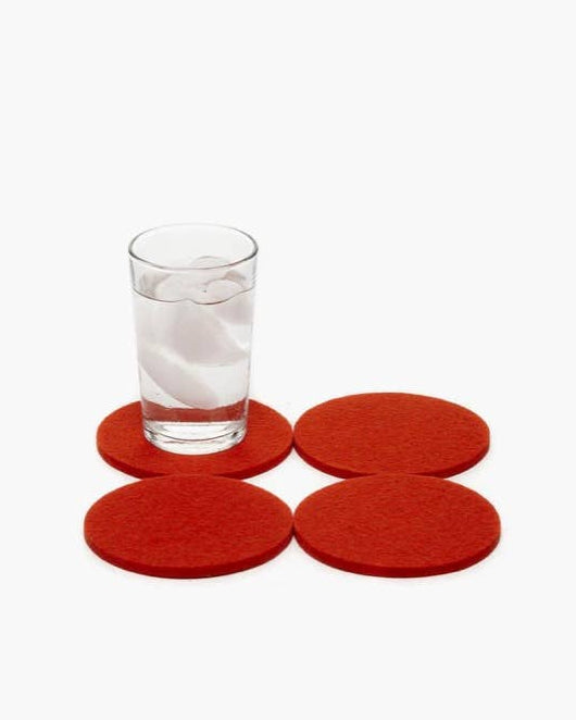 Set of four red coasters, one with a glass of water on top, on a white background