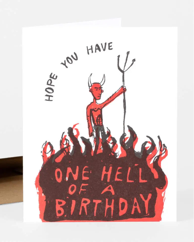 A folded birthday card with a cartoonish illustration of a devil on it standing on flames, along with text that reads &